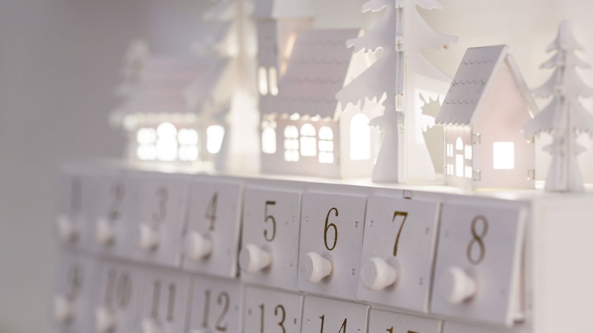 Hvit adventskalender i tre med nummererte skuffer og små hus på toppen