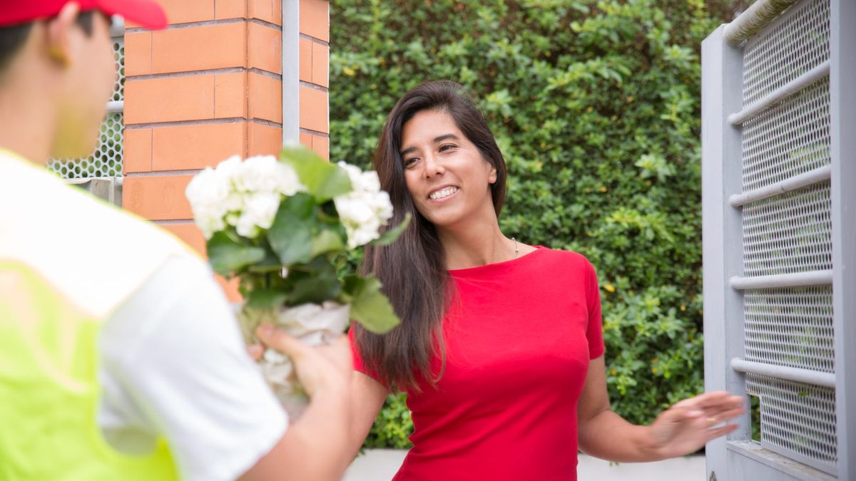 Bud som leverer en bukett med hvite blomster til en kvinne ved porten