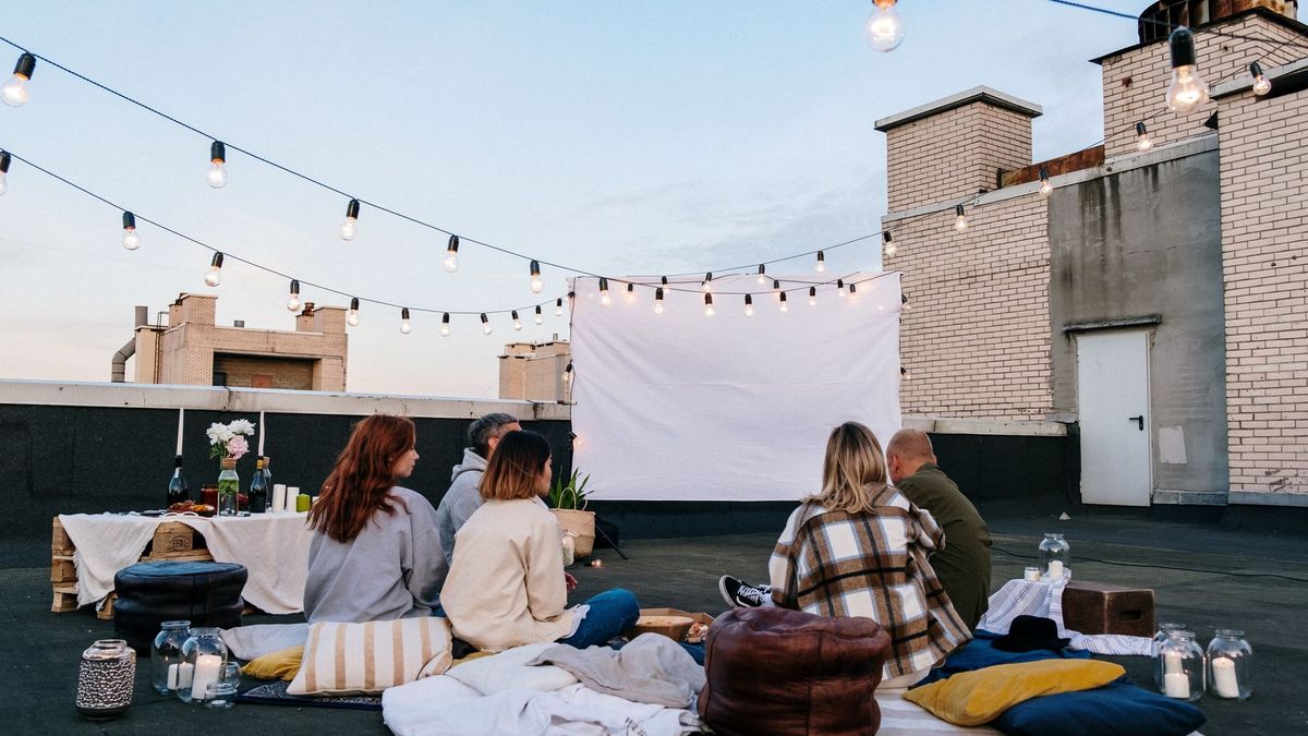 Utekino på en takterrasse med lerret, lyslenker og folk på pledd