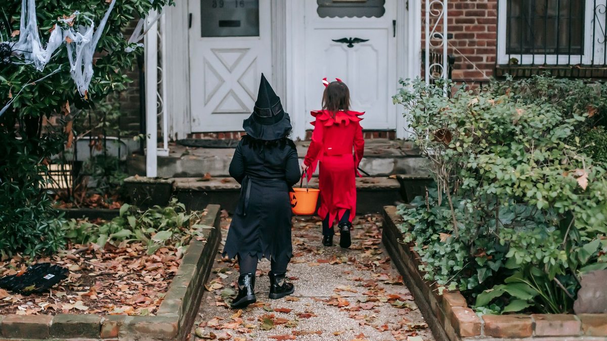 To barn i halloweenkostymer som går mot en pyntet inngangsdør