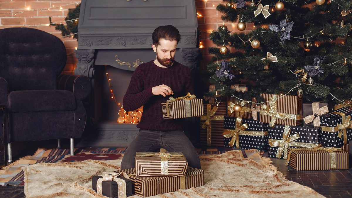 Mann som pakker opp gaver foran juletreet