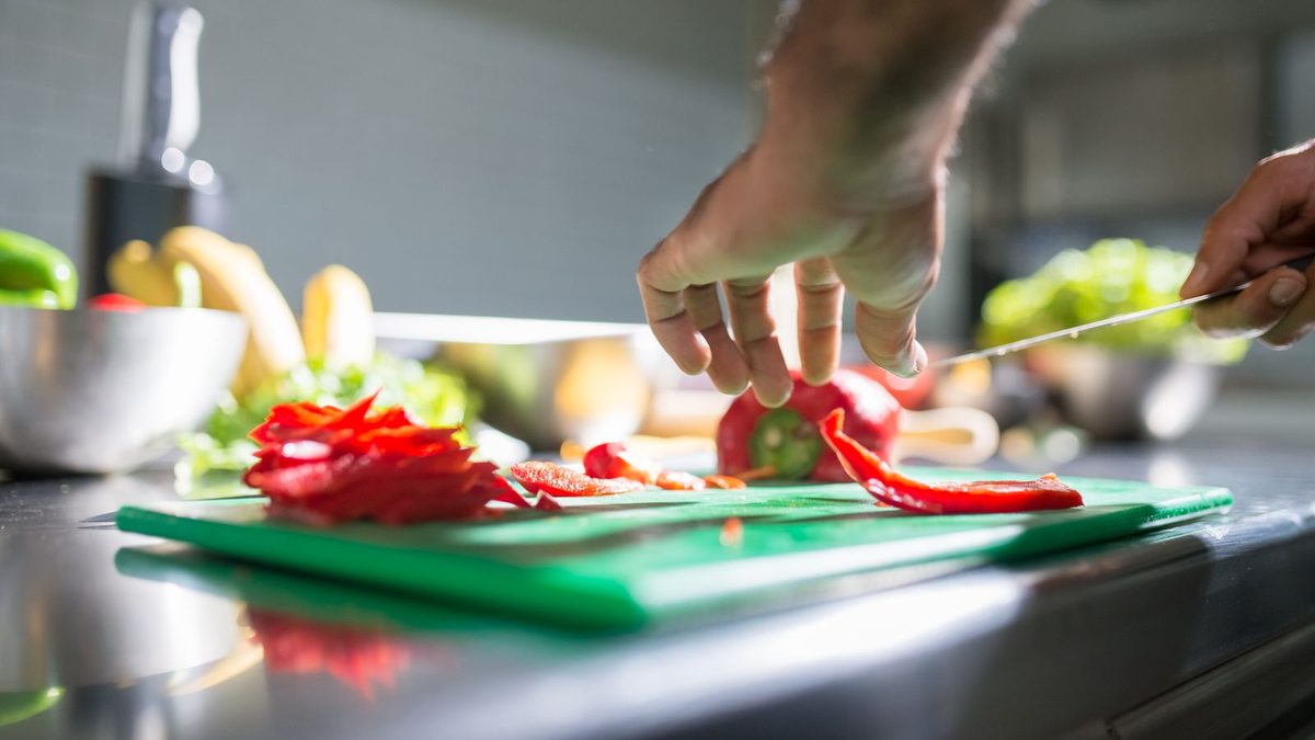 Hender som skjærer rød paprika i strimler på en skjærefjøl