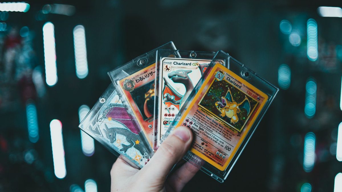 Hånd som holder fire Pokémon-kort i plastlommer, blant dem et Charizard-kort