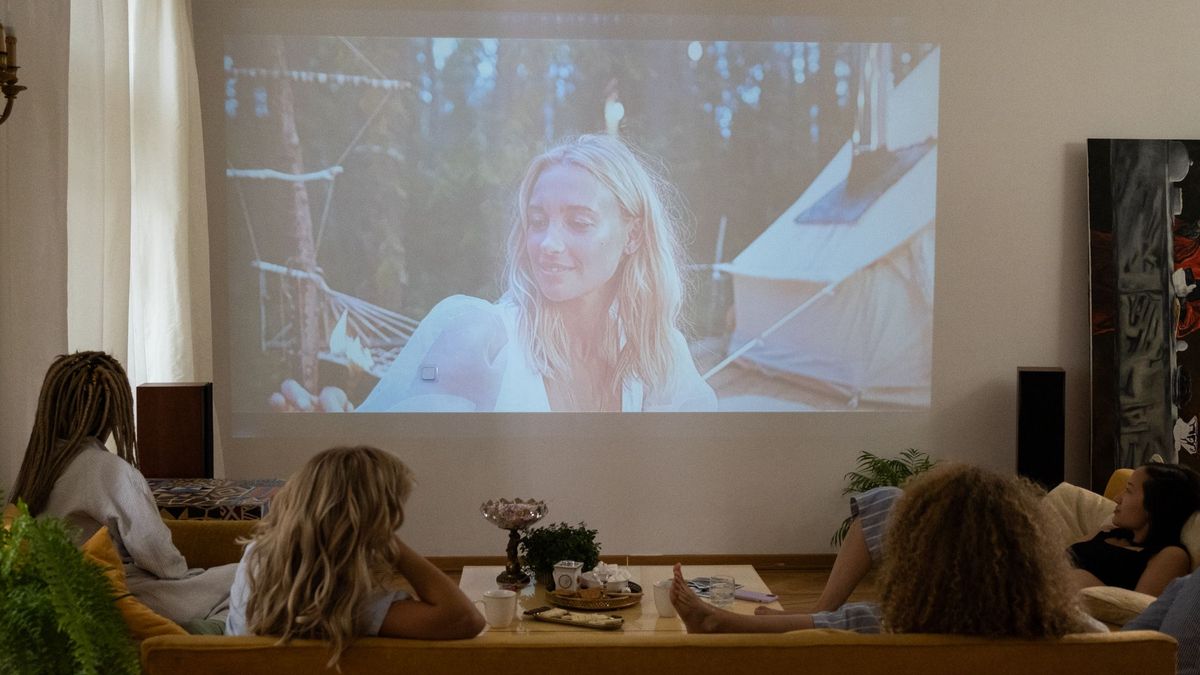 Venner i sofaen som ser film projisert på stueveggen