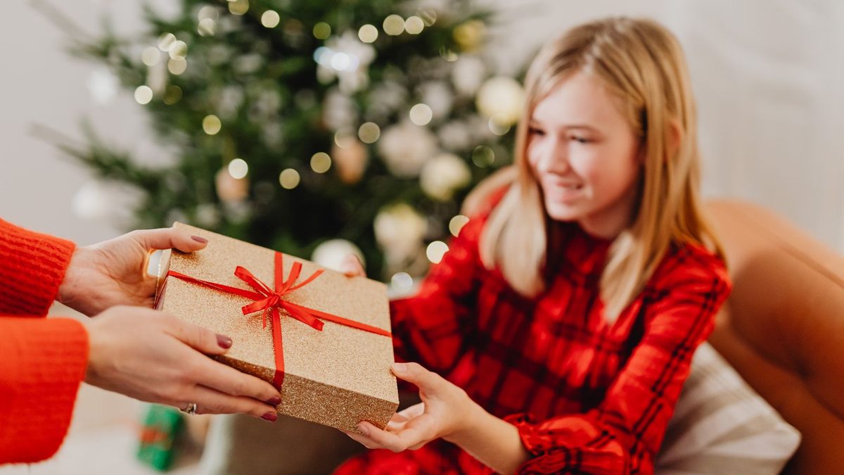Tenåringsjente som smiler og tar imot en innpakket gave foran juletreet
