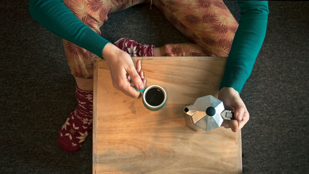 Føtter i ullsokker ved et trebrett med kaffekopp og espressokanne