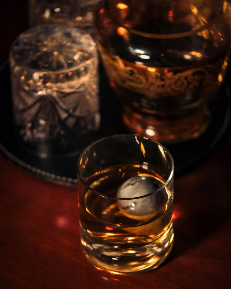 Whiskyglass med en stor iskule på et mørkt brett