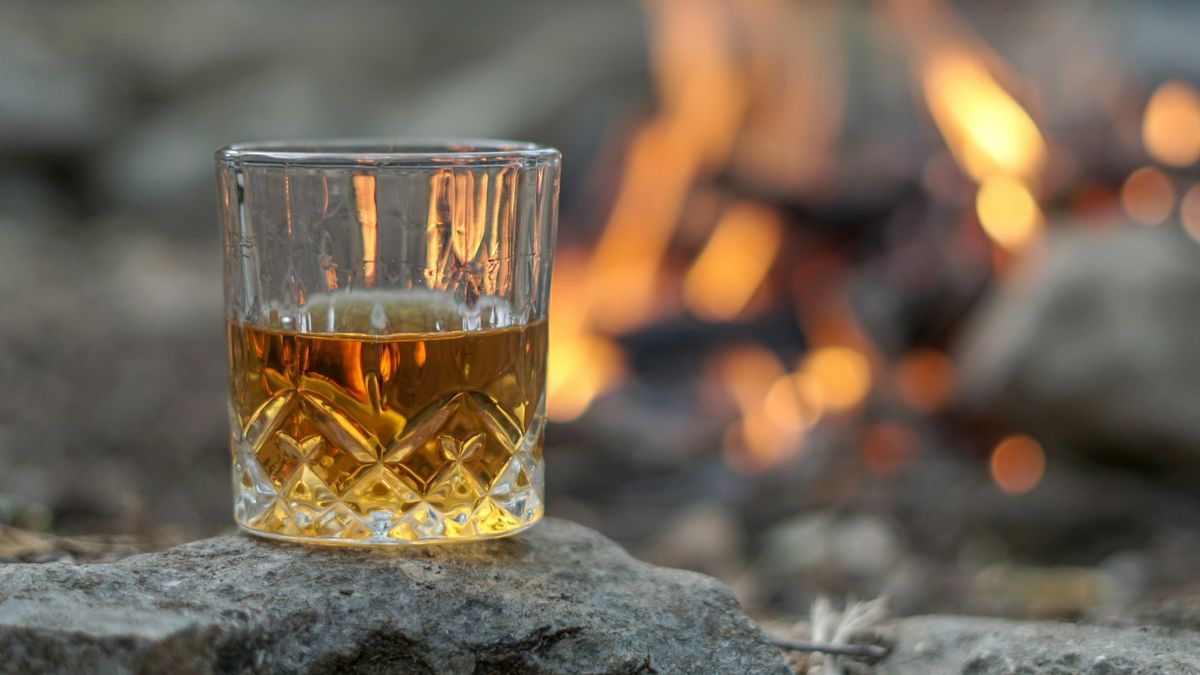 Krystallglass med whisky uten is på en stein ved et bål